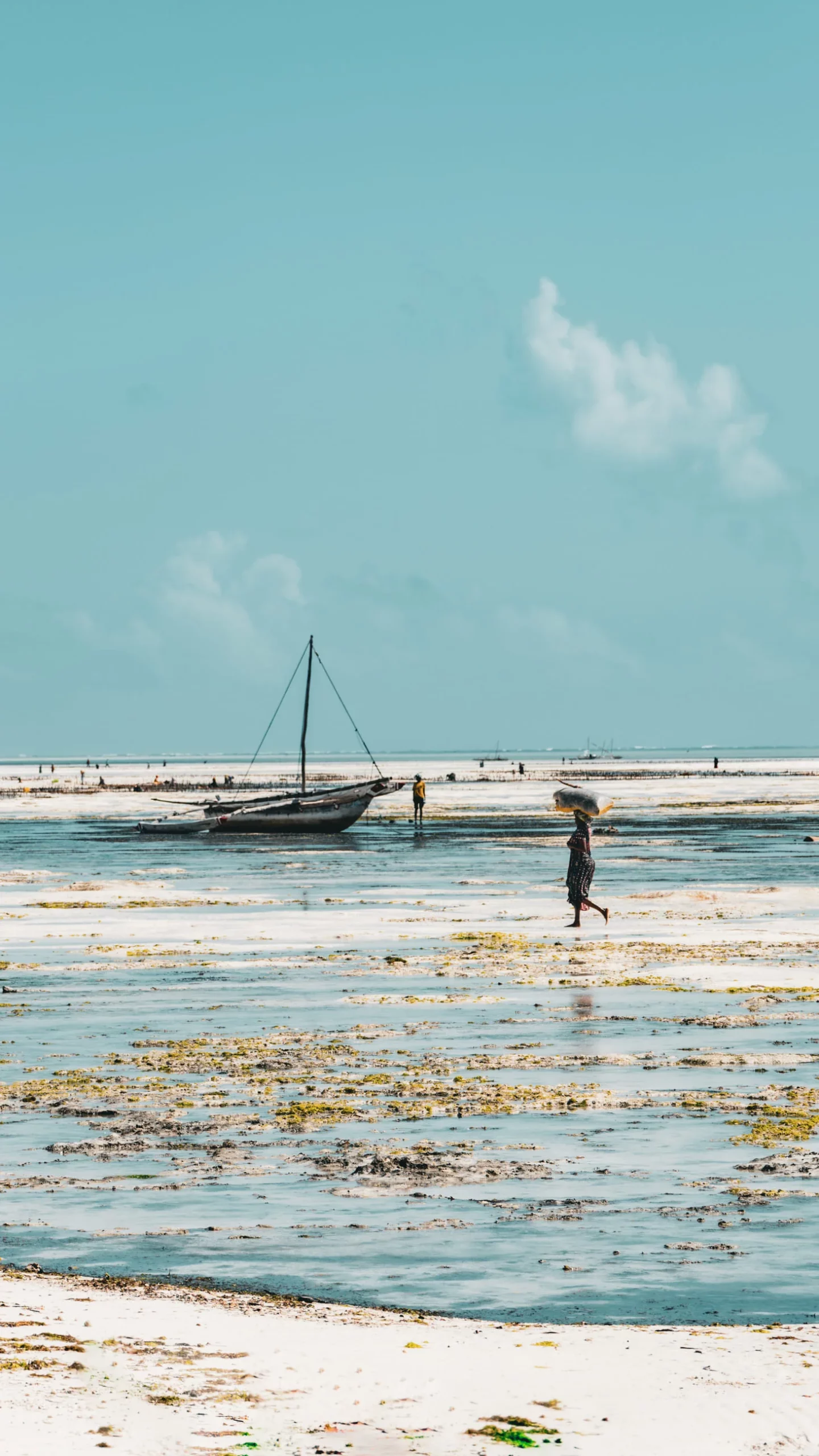 Traditional sailing boat and people walking on the beach at low tide on Zanzibar's south-east coast