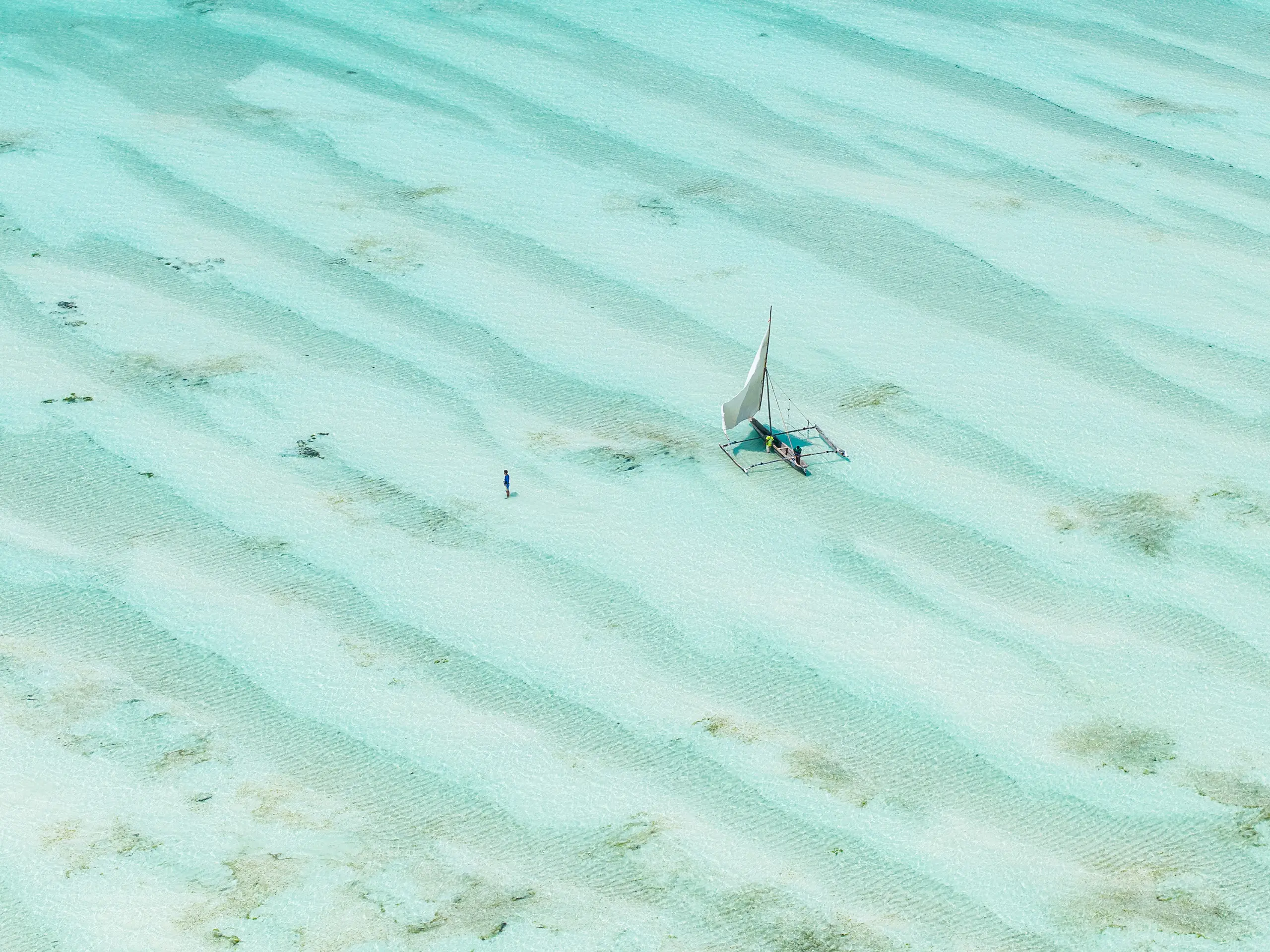 Aerial view of a traditional sailing dhow on shallow turquoise water with sand ripples, Zanzibar
