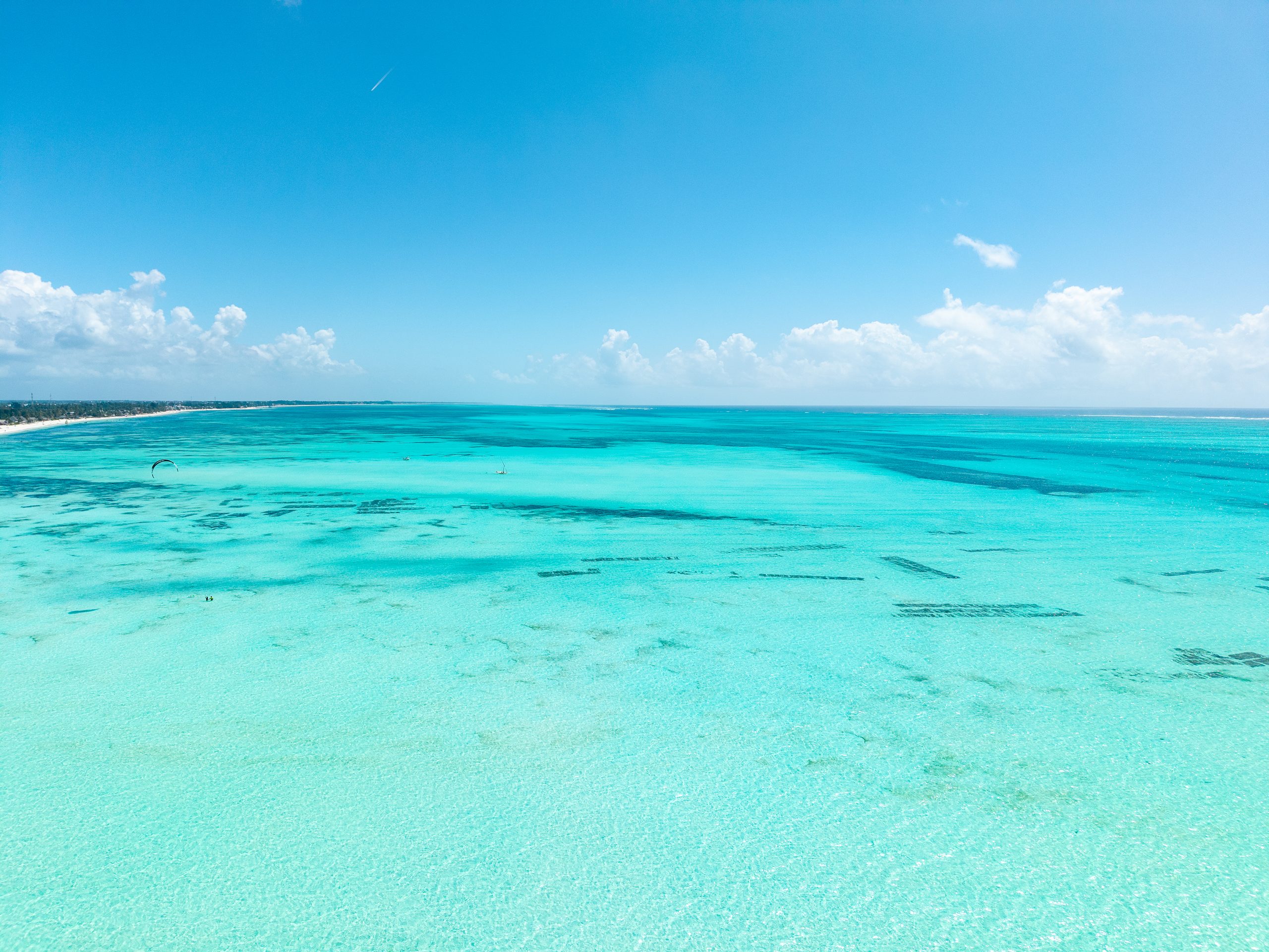 Turquoise lagoon in Jambiani, Zanzibar, as the tide comes in, with seaweed farms below the surface and the reef on the horizon